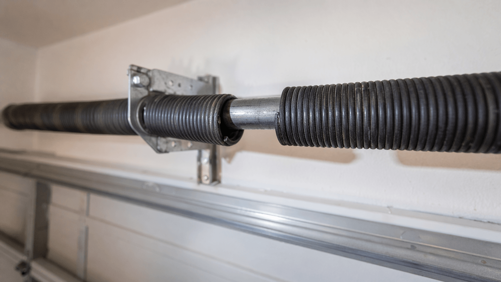 Close-up of a snapped torsion spring on a residential garage door showing the distinctive 2-inch gap in the coils where it has separated — the classic visual sign of a broken garage door spring in an Arizona home